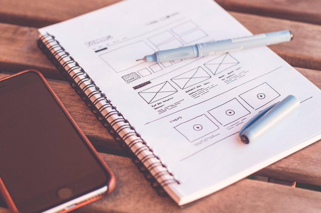 Maquette d'un site web dessinée à la main dans un carnet, près d'un téléphone